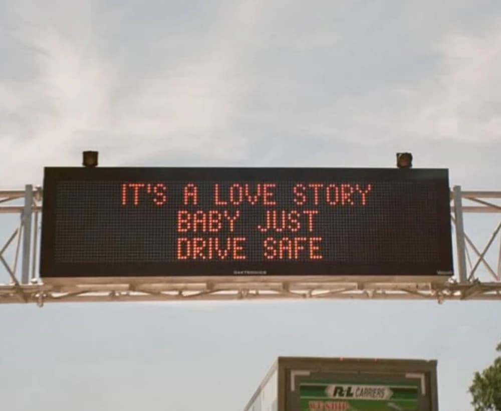Highway sign reading It's a love story, baby, just drive safe