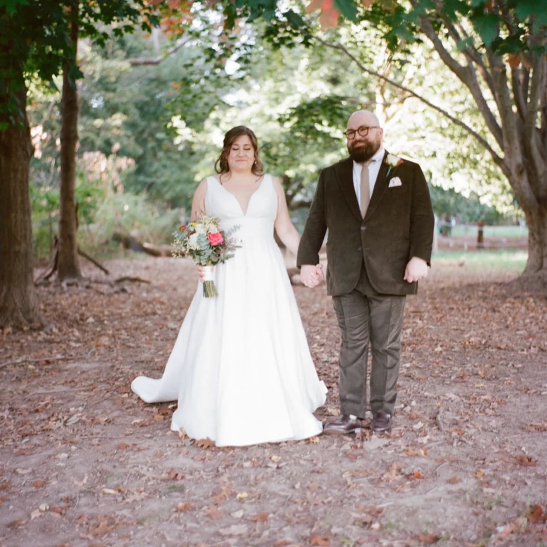 A bride and groom holding hands under autumn trees